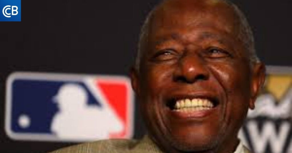 An older person smiling in front of a baseball logo.